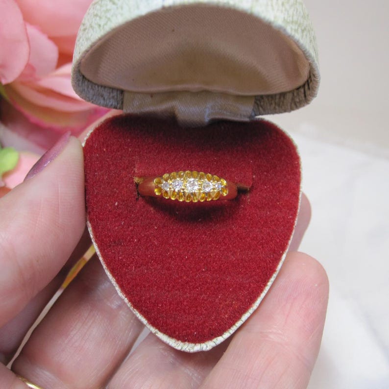 May include: A gold ring with a row of small diamonds set in the band. The ring is in a red velvet heart-shaped box.