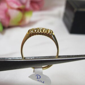 May include: A gold band ring with a row of small diamonds set in the band. The ring is held by a pair of tweezers.