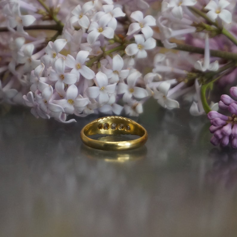 May include: A gold band ring with a row of small clear stones set in the band.