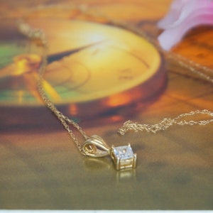 May include: A gold chain necklace with a square-shaped pendant featuring a clear gemstone.