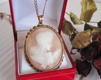 May include: A gold chain necklace with a cameo pendant featuring a carved image of a woman's profile. The cameo is set in a gold frame with a detailed design.