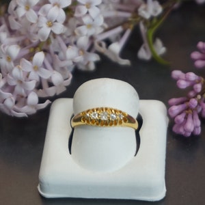 May include: A delicate gold band ring with five small diamonds set in a row. The ring is displayed on a white ring holder.