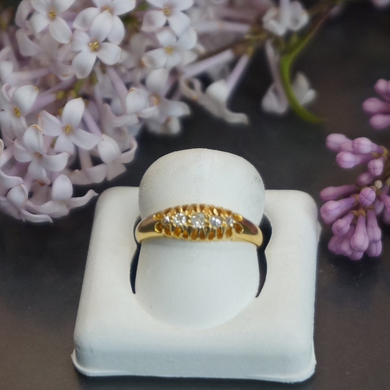 May include: A delicate gold band ring with five small diamonds set in a row. The ring is displayed on a white ring holder.