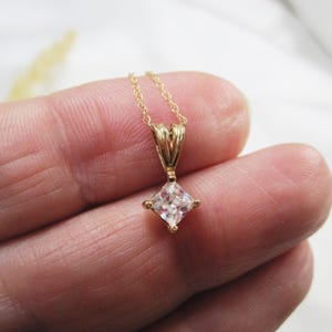 May include: A gold chain necklace with a square-shaped pendant featuring a clear cubic zirconia stone.