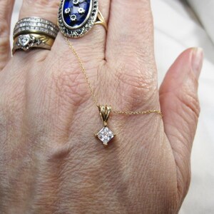 May include: A gold chain necklace with a square-shaped pendant featuring a clear, faceted gemstone.