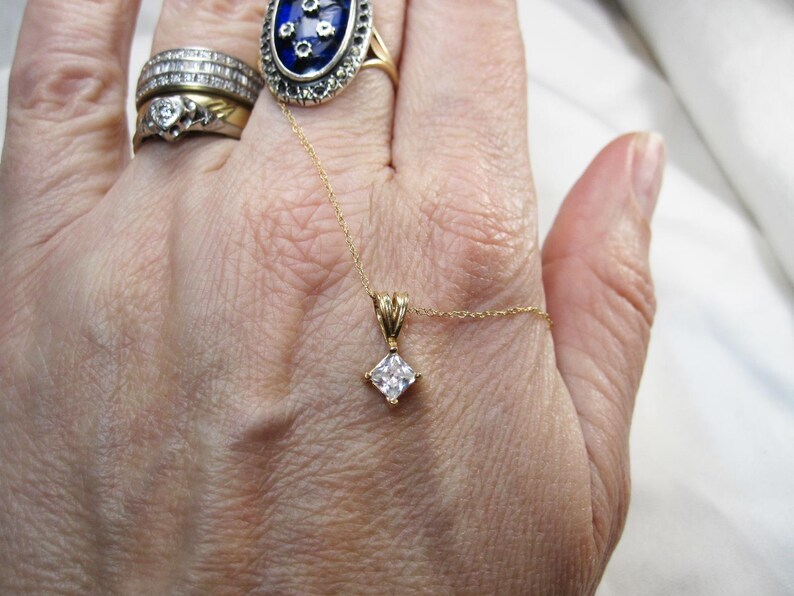May include: A gold chain necklace with a square-shaped pendant featuring a clear, faceted gemstone.