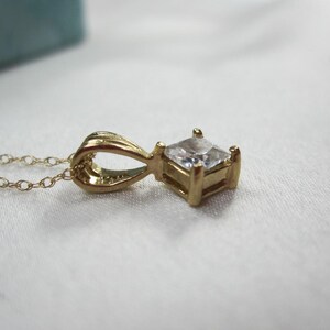 May include: A gold chain necklace with a pendant featuring a square-shaped clear gemstone.