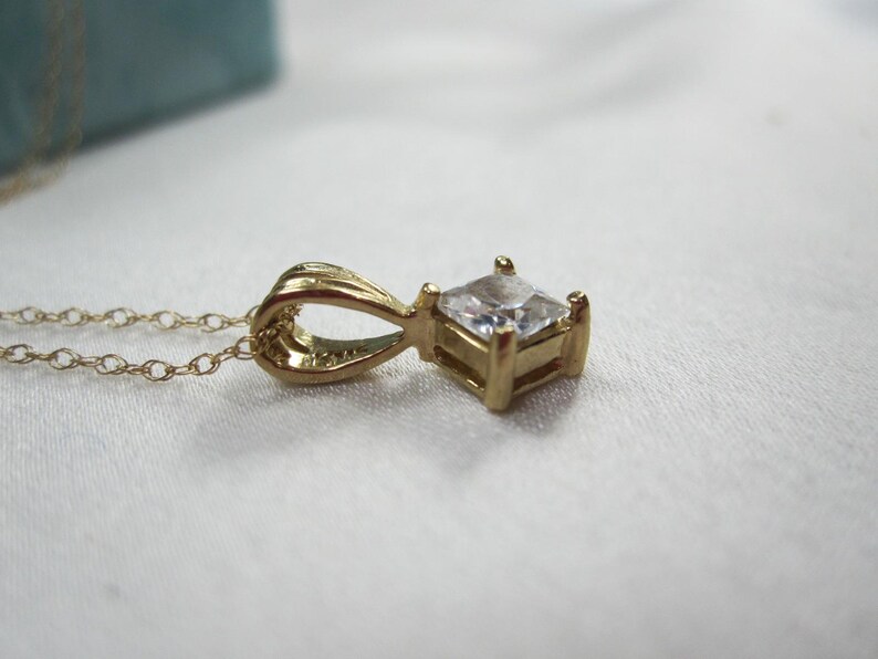 May include: A gold chain necklace with a pendant featuring a square-shaped clear gemstone.