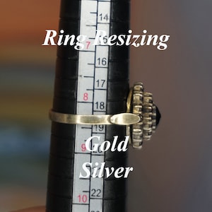 Könnte beinhalten: Ein silberner Ring mit einem schwarzen Stein und einer goldenen Band wird auf einem Ringgrößenmesser gezeigt. Der Ringgrößenmesser zeigt die Größen 7 bis 10. Der Text "Ring Resizing Gold Silver" ist auf dem Bild gedruckt.