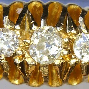 May include: A gold ring with three round diamonds set in a textured band. The diamonds are clear and sparkly.
