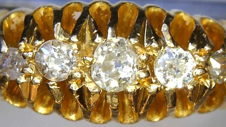 May include: A gold ring with three round diamonds set in a textured band. The diamonds are clear and sparkly.