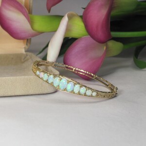 Puede incluir: Un brazalete de oro con una fila de ópalos ovalados engastados en un delicado diseño de filigrana.