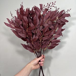 May include: A bunch of burgundy artificial eucalyptus stems with small berry-like accents.