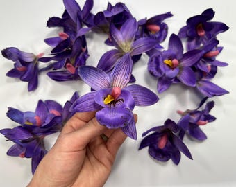 May include: A collection of purple and pink artificial orchid flowers. The flowers have a realistic appearance and are perfect for adding a touch of elegance to any space.
