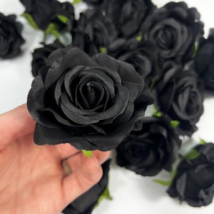 May include: A bunch of black silk roses with green stems. The roses are arranged in a cluster and are all facing the same direction.