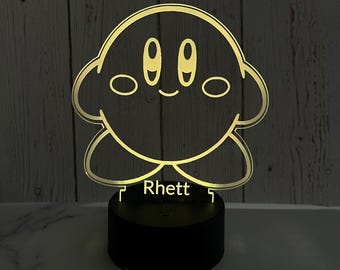 May include: A yellow light-up nightlight shaped like a cartoon character with the name "Rhett" printed below. The character has large eyes and a smiling mouth.