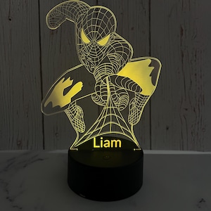 May include: A yellow 3D printed night light shaped like Spiderman with a web design. The light has a black base with the name "Liam" printed on it.