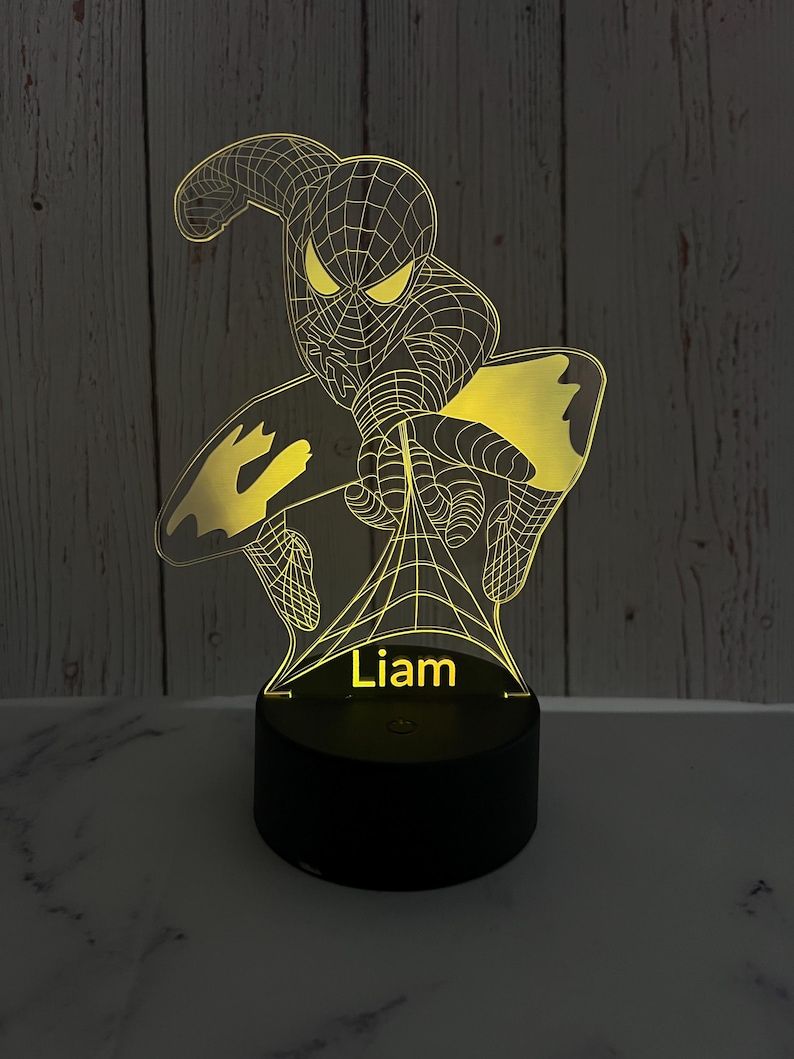 May include: A yellow 3D printed night light shaped like Spiderman with a web design. The light has a black base with the name "Liam" printed on it.