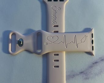 May include: A pink Apple Watch band with a stethoscope and heartbeat design. The band is personalized with the name "Emma".