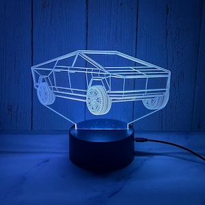 May include: A blue 3D printed night light shaped like a Tesla Cybertruck. The light is on a black base and is plugged in with a black cord.