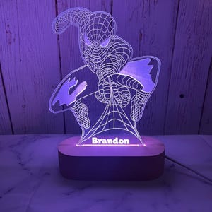 May include: A white and purple night light with a Spiderman design and the name "Brandon" on the base.