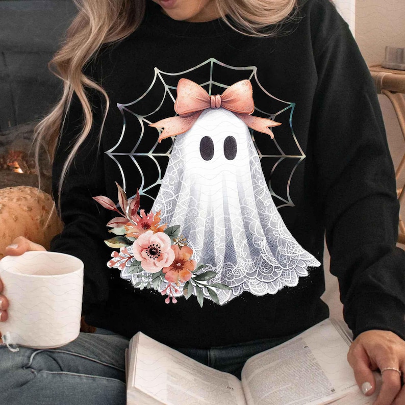 May include: Black sweatshirt with a white ghost wearing a pink bow and lace, surrounded by a spiderweb. The ghost is holding a bouquet of pink and white flowers.