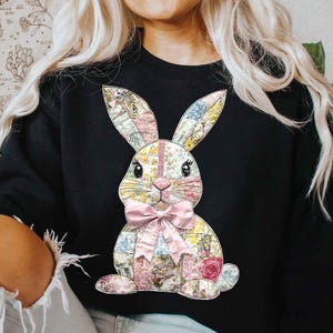 May include: Black sweatshirt featuring a patchwork bunny design. The bunny has a pink bow and is made from various floral fabrics.