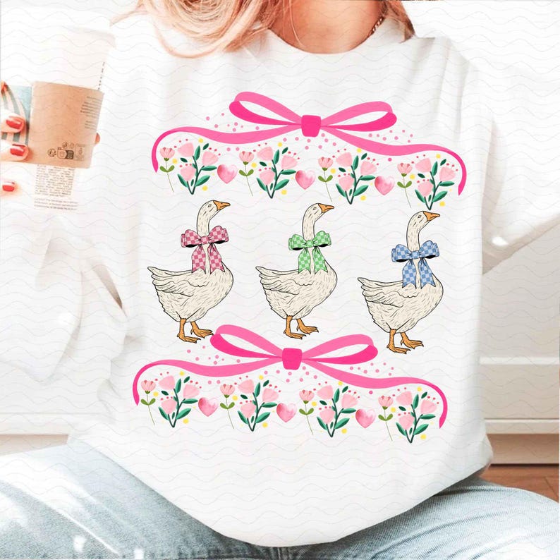 May include: White sweatshirt featuring three geese with colorful bowties. Pink bows and floral accents frame the geese. The geese have orange beaks and feet. The design is a whimsical, springtime theme.
