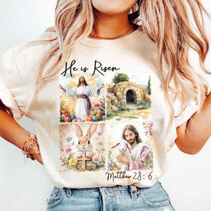Puede incluir: Una camiseta blanca con un collage de imágenes con temática de Pascua. Las imágenes incluyen a Jesús, una tumba, un conejito y un cordero. El texto "He is Risen" y "Matthew 28:6" también están incluidos.