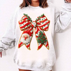 Pode incluir: Um moletom cinza claro com um grande e detalhado design de la&ccedil;o de Natal. O la&ccedil;o &eacute; listrado em vermelho e branco com detalhes verdes, um rosto de Papai Noel e uma &aacute;rvore de Natal. O design est&aacute; centralizado na frente.