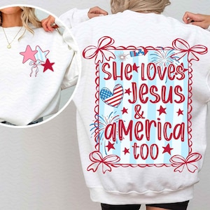 May include: White sweatshirt with a patriotic design. The back features the text "She Loves Jesus & America Too" in red, with a heart in the American flag colours. The front has star graphics. Ribbons and fireworks complete the design.