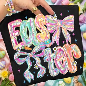 May include: Black t-shirt with the word "EASTER" in large, colorful bubble letters. The letters are decorated with bows, daisies, and Easter eggs. The design has a pastel color scheme with pink, blue, yellow, and orange.