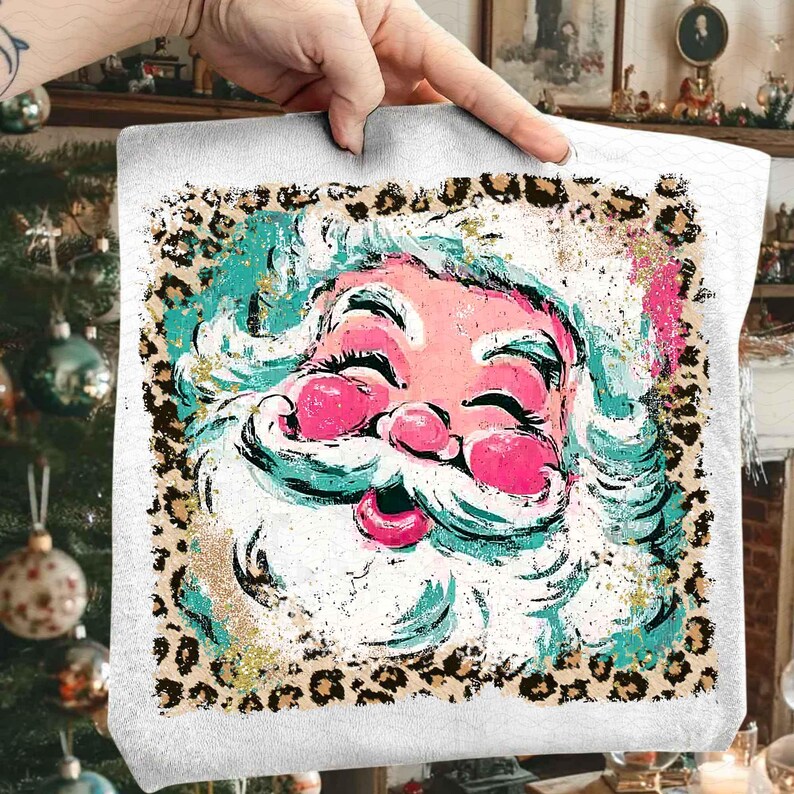 May include: A white tote bag featuring a colorful Santa Claus face with a pink nose and lips, and a white beard. The Santa face is surrounded by a leopard print border. The Santa's face has turquoise and gold accents.