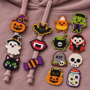 May include: A collection of embroidered Halloween-themed patches featuring a pumpkin, ghost, black cat, bat, vampire lips, candy, candy corn, Frankenstein, cauldron, vampire, tombstone with RIP, skull, cat in pumpkin, and a jar of eyeballs.