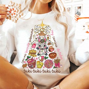 May include: White long-sleeve sweatshirt with a Christmas tree design featuring a donkey, a star, and the text "voy camino de belen con mi burrito sabanero tuki tuki tuki tuki".