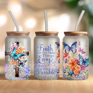 May include: Three stainless steel tumblers with lids and straws. Each tumbler features a different design with butterflies, flowers, and a cross. The middle tumbler has the text "Faith Does Not Make Things Easy It Makes Them Possible Luke 1:37".