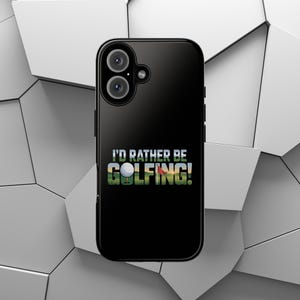 Peut inclure: Coque de téléphone noire avec le texte "I'D RATHER BE GOLFING!". Le design présente une balle de golf sur un tee avec un arrière-plan vert et marron. La coque de téléphone a un système à double caméra.