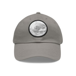 May include: A gray baseball cap with a black and white circular patch featuring a stylized image of a face.