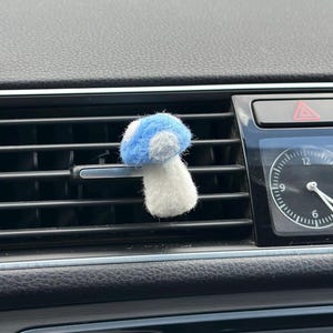 May include: A blue and white felt mushroom car air freshener hanging from a car's air vent.