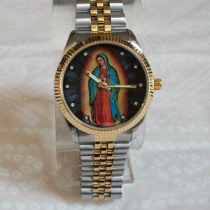 May include: A gold and silver two-tone wristwatch with a black face featuring a colorful image of the Virgin Mary. The watch has a stainless steel band.
