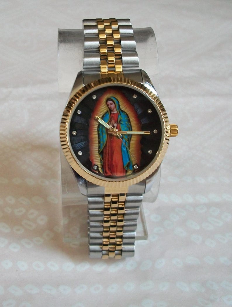 May include: A gold and silver two-tone wristwatch with a black face featuring a colorful image of the Virgin Mary. The watch has a stainless steel band.