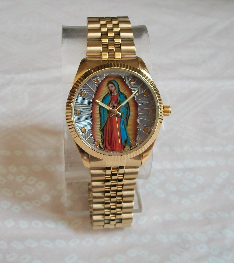 May include: A gold-tone wristwatch with a round face featuring a colorful image of the Virgin Mary. The watch has a gold-tone metal band.