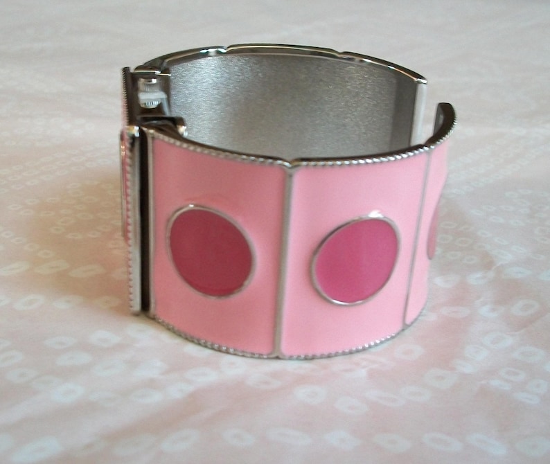 May include: A silver bangle bracelet with a pink enamel design featuring three large circles. The bracelet is open and ready to be worn.