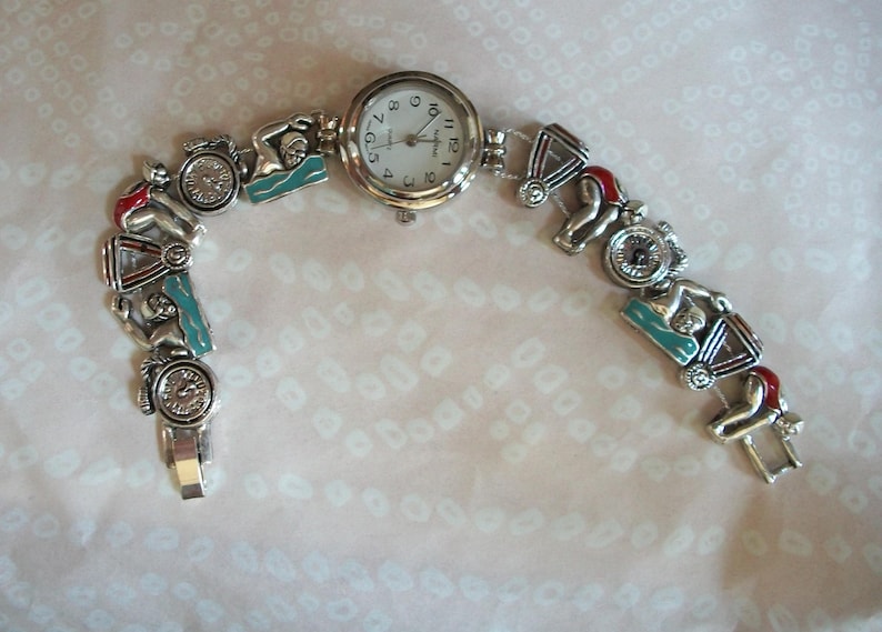 May include: A silver watch with a white face and black numbers. The watch band is made of silver and has charms of swimmers and lifeguards.