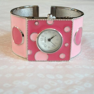 May include: A pink and silver bangle watch with a white face and black numbers. The watch has a polka dot design.
