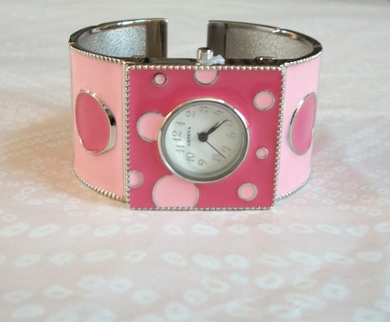 May include: A pink and silver bangle watch with a white face and black numbers. The watch has a polka dot design.