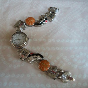 May include: A silver watch with a white face and black hands. The watch band is decorated with basketballs, sneakers, and the number 23.