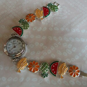 May include: A silver wristwatch with a white face and black numbers. The watch band is made of silver links and features colorful enamel charms of fruit, including watermelon, pineapple, orange, and banana.