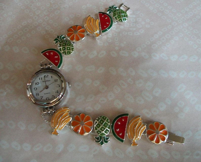 May include: A silver wristwatch with a white face and black numbers. The watch band is made of silver links and features colorful enamel charms of fruit, including watermelon, pineapple, orange, and banana.