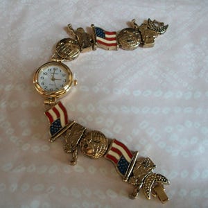 May include: A gold-tone watch bracelet with a white face and black hands. The bracelet features a repeating pattern of American flags, globes, and stars.